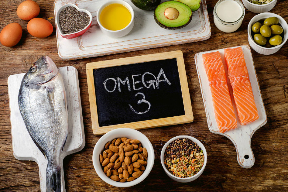 Na drewnianym blacie znajdują się różnorodne źródła kwasów omega-3, w tym ryba, łosoś, orzechy, awokado oraz nasiona chia, podkreślając zdrowe składniki diety.