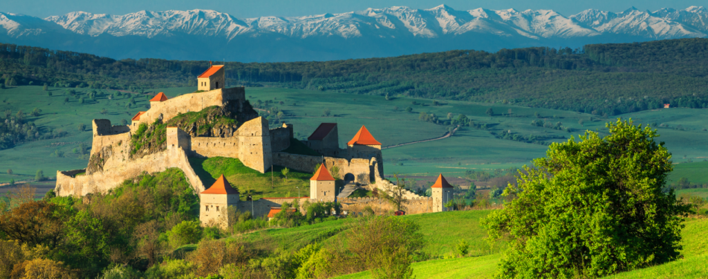 Malowniczy zamek otoczony zielonymi wzgórzami i majestatycznymi górami w tle, doskonały przykład średniowiecznej architektury.