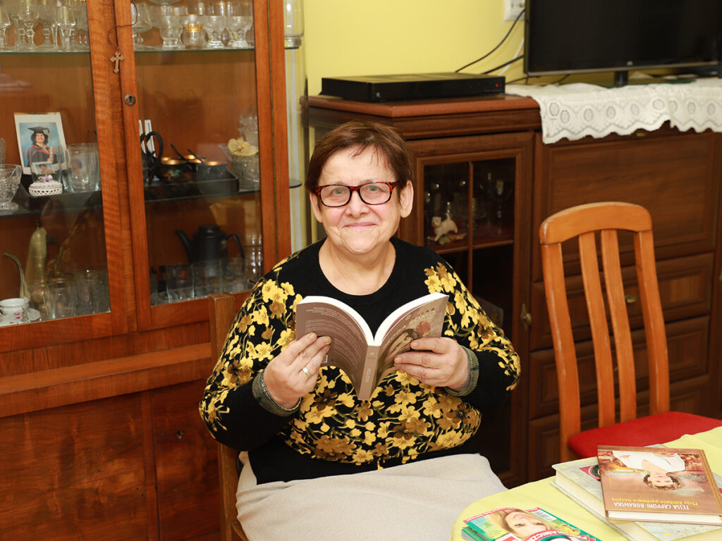 Osoba czytająca książkę w przytulnym wnętrzu z drewnianymi meblami i różnorodnymi przedmiotami na półkach.