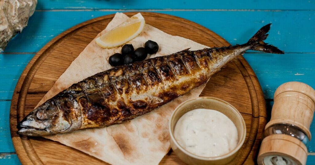 Grillowana ryba podana z cytryną, oliwkami i sosem na talerzu z naturalnego drewna.