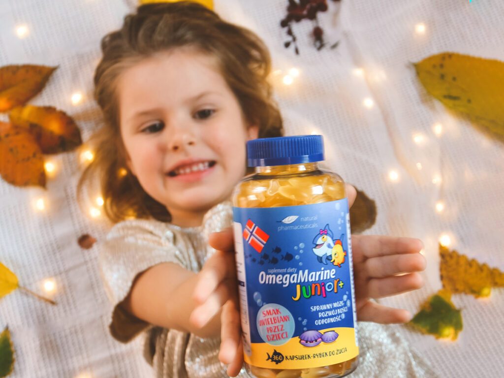 Dziewczynka trzymająca butelkę suplementu diety OmegaMarine Junior+, który wspiera zdrowie dzieci dzięki przyjemnemu smakowi.