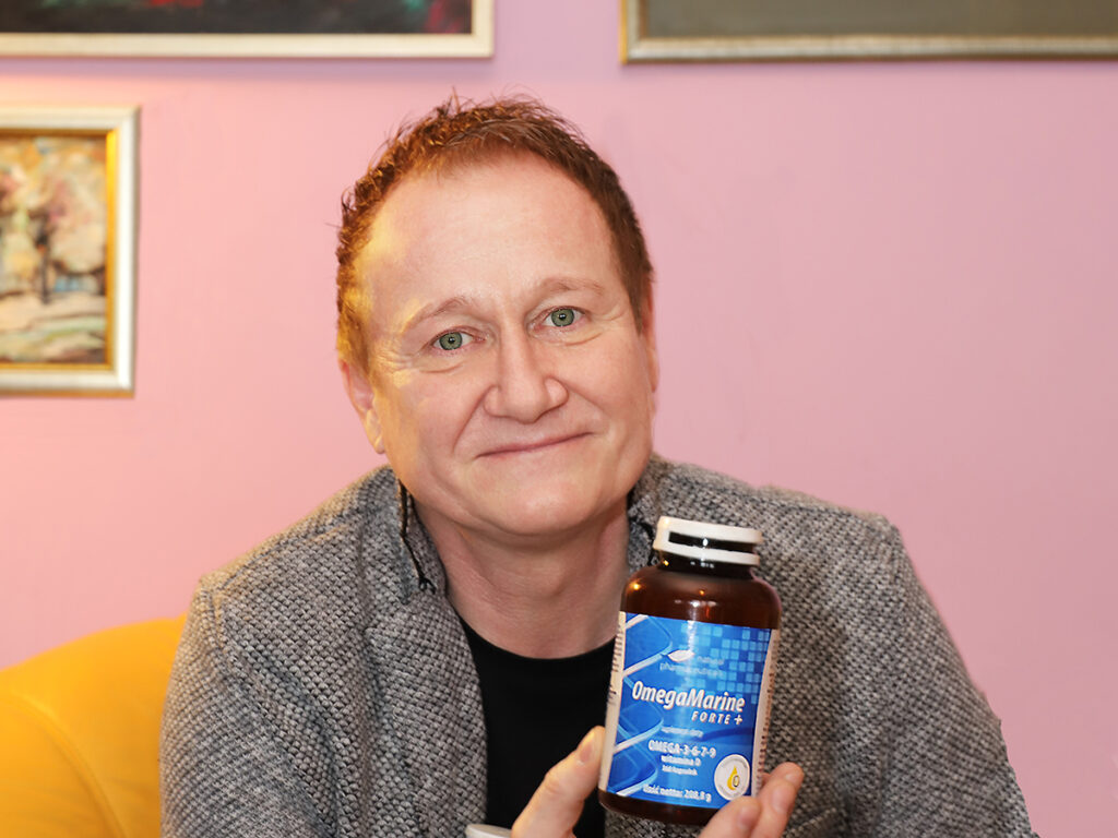 Mężczyzna trzymający produkt OmegaMarine Forte+ w białym opakowaniu, promujący korzyści zdrowotne suplementów omega-3.