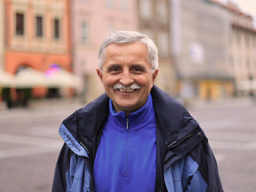 Uśmiechnięty mężczyzna w niebieskiej odzieży na tle miejskiego krajobrazu.