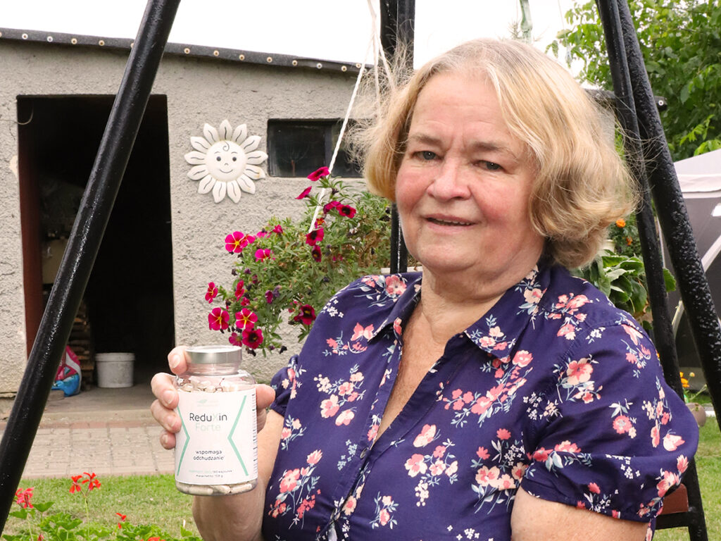 Kobieta trzymająca słoik z produktem o nazwie ReduXin, na tle kolorowych kwiatów i szarego budynku.