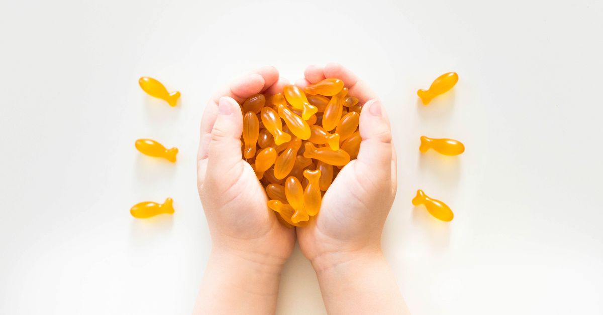 Dziecięce ręce trzymające garść żelek z kwasami omega-3 w kształcie rybek.