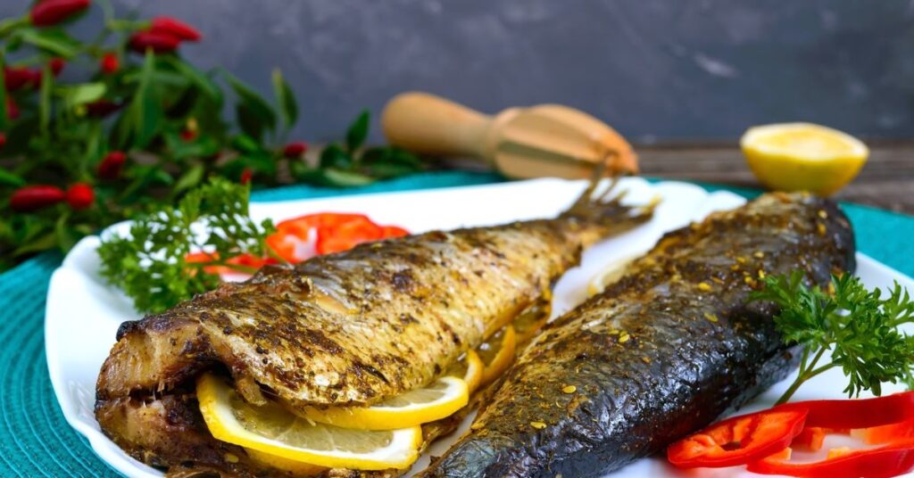 Grillowana ryba z cytryną, podana na talerzu z świeżymi ziołami i warzywami, stanowi smaczną i zdrową propozycję na obiad.