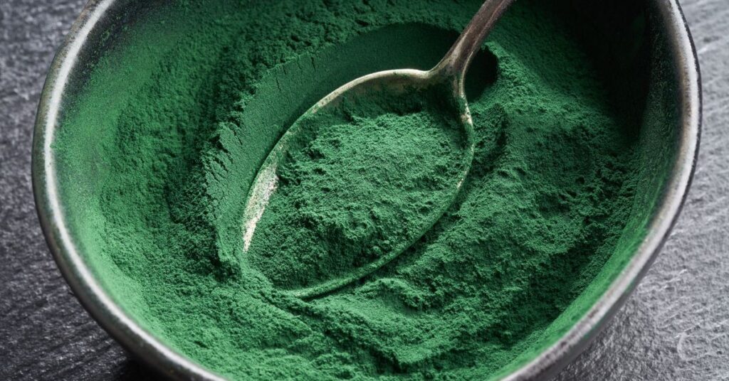 Zielony proszek spiruliny umieszczony w czarnej misce ze srebrną łyżką, idealny do suplementacji zdrowotnej i odżywiania.