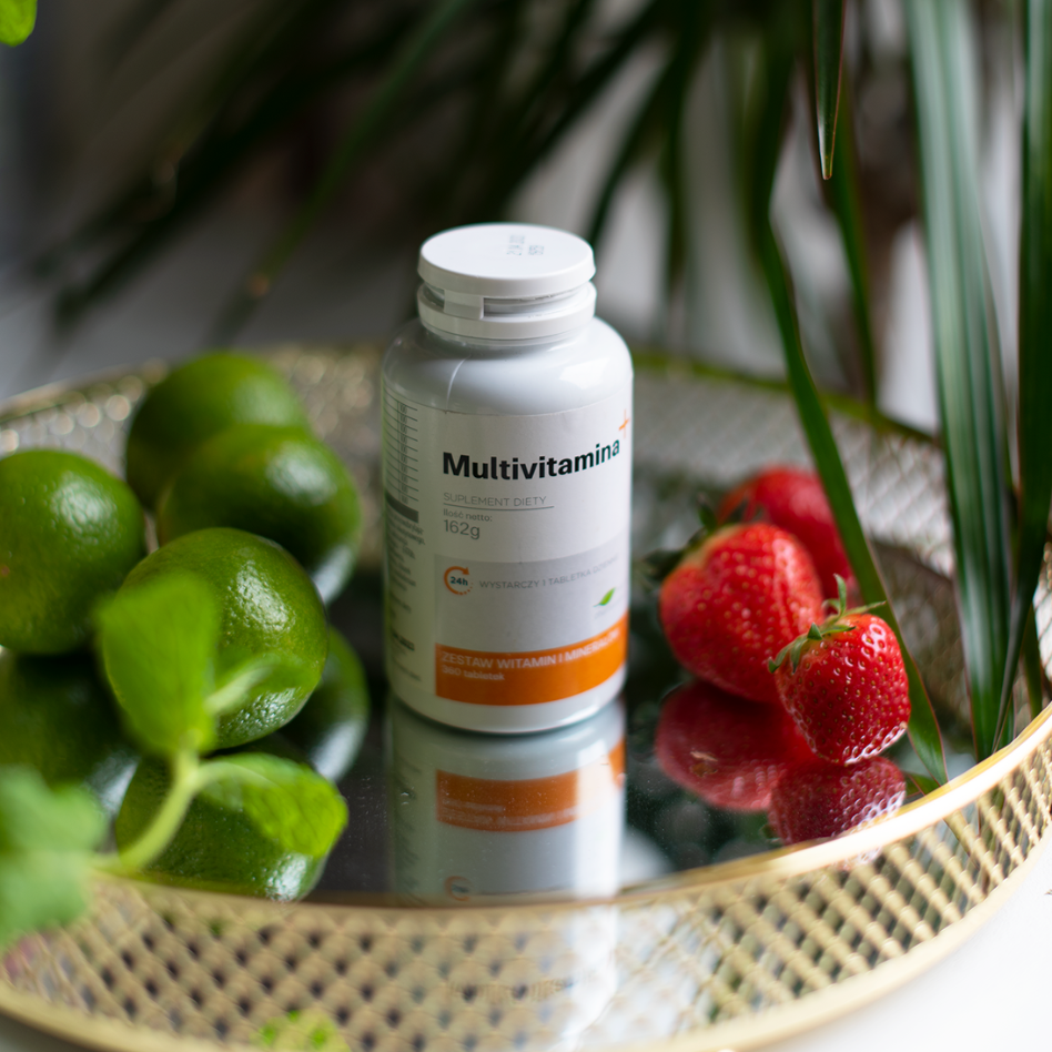 Butelka multivitaminowa otoczona świeżymi limonkami i truskawkami na lustrzanej tacy.