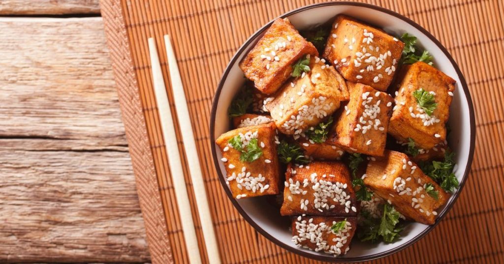 Aromatyczne kawałki tofu zapiekane z sezamem i świeżymi ziołami podane w eleganckiej misce na bambusowym tle.
