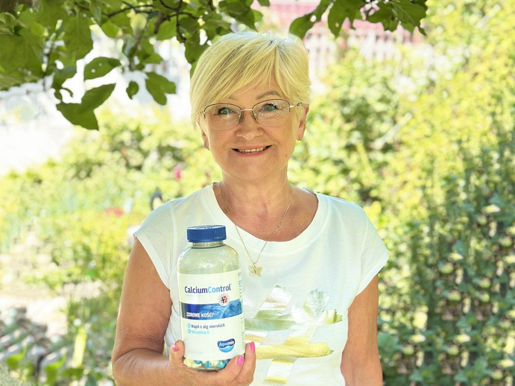 Kobieta w białej koszulce trzyma butelkę z suplementem CalciumControl, promując zdrowie kości w otoczeniu zieleni.