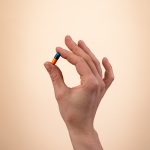 Ręka trzymająca kolorową kapsułkę suplementu Movisan Collagen II na neutralnym tle, symbolizująca zdrowie i suplementację.
