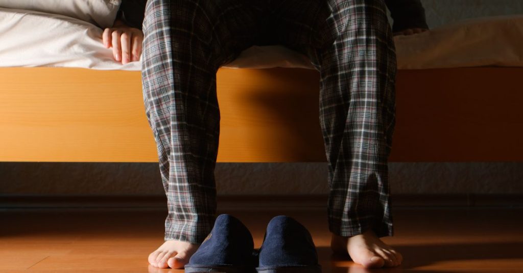 Osoba w piżamie siedzi na łóżku, przygotowując się do porannej rutyny w domu.