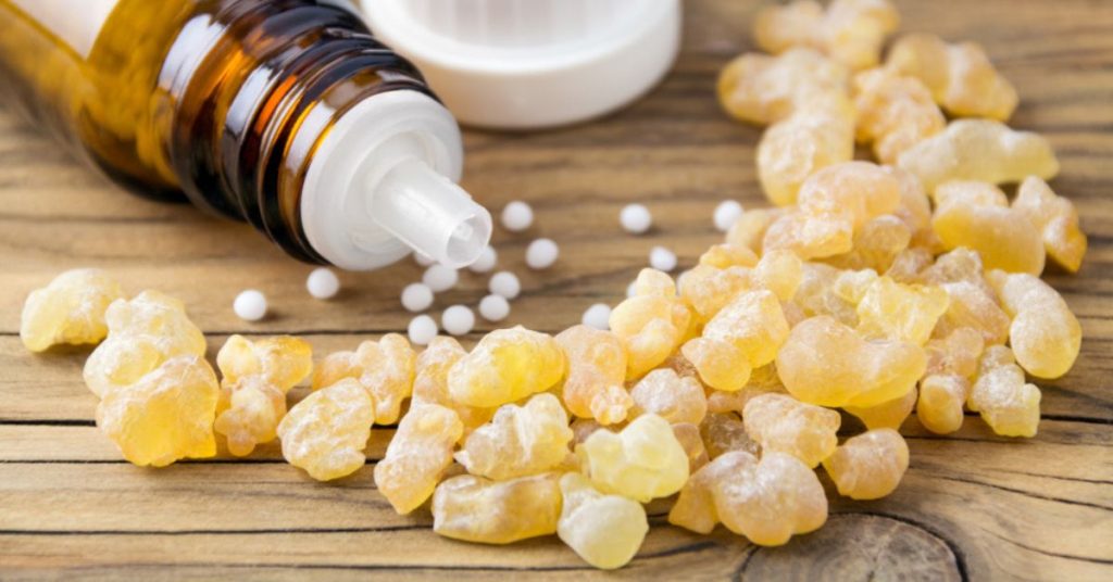 Na drewnianym blacie znajdują się kawałki żywicy oraz buteleczka z płynem do aromaterapii, co sugeruje zastosowanie naturalnych składników w terapii zdrowotnej.