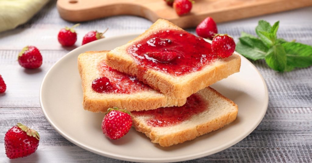 Talerz z kromkami chleba z dżemem truskawkowym, otoczony świeżymi owocami i liśćmi mięty, idealny na szybkie i smaczne śniadanie.